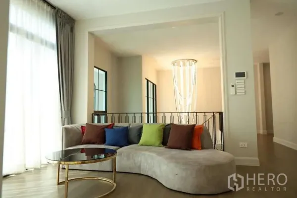 独立式住宅 出租或出售在Saphan Sung, Bangkok - 明亮起居角，弧形沙发与彩色抱枕，楼梯吊灯可见