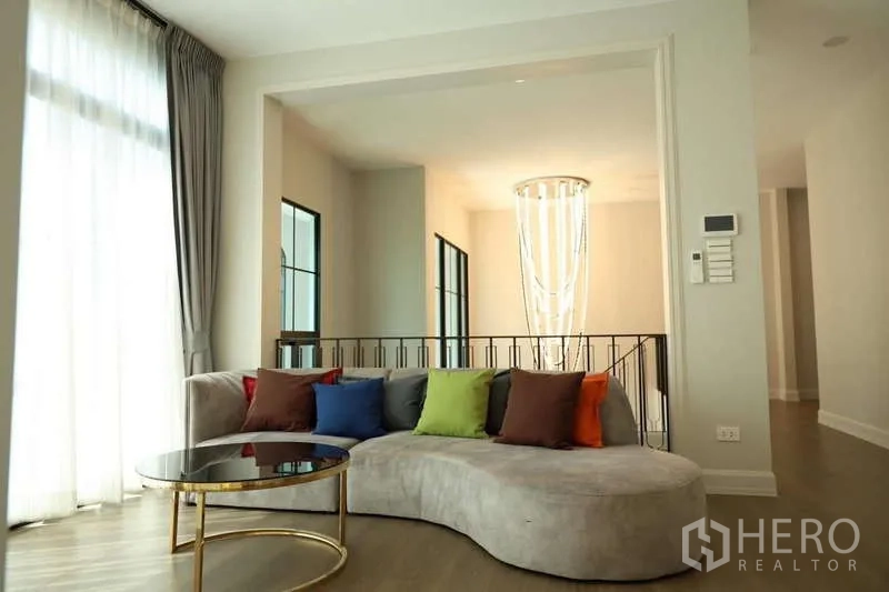 独立式住宅 出租或出售在Saphan Sung, Bangkok - 明亮起居角，弧形沙发与彩色抱枕，楼梯吊灯可见