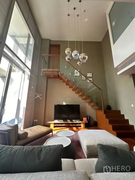 Condominium for rent or sale in Sathon, Bangkok - Living area showcasing floating wooden stairs, pendant lights, and expansive glazing.