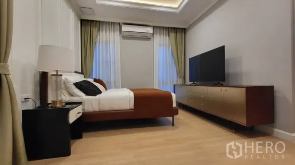 Detached House for rent or sale in Saphan Sung, Bangkok - Minimalist bedroom with large TV console, soft drapes, and warm wood flooring.