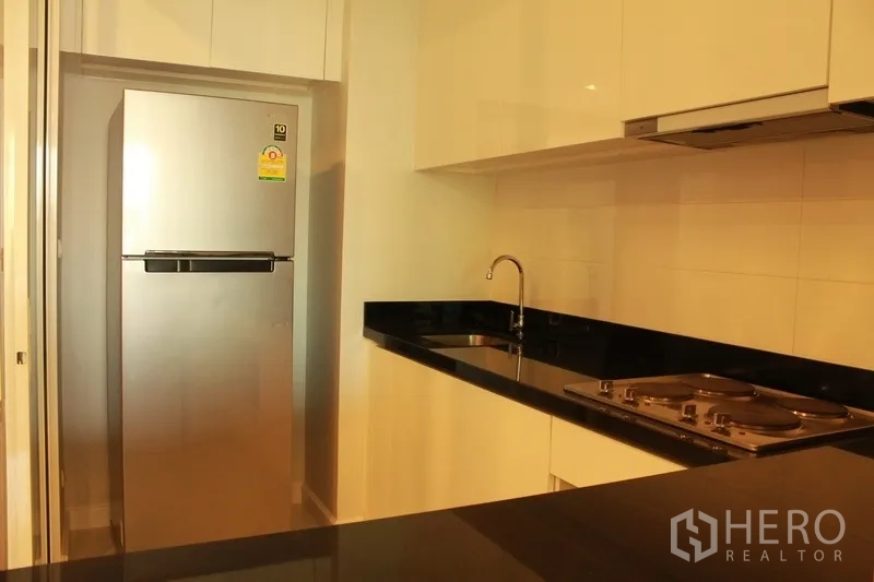 คอนโด ให้เช่าในWatthana, Bangkok - ห้องครัวบิวท์อินเคาน์เตอร์หินแกรนิตสีดำ เตาไฟฟ้า ตู้เย็นสแตนเลส และตู้สีขาวเงา