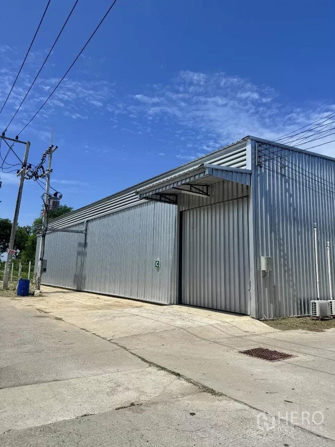 Warehouse for rent in Bang Lamung, Chon Buri - Close exterior of a unit with sliding metal door, canopy and roadside access.