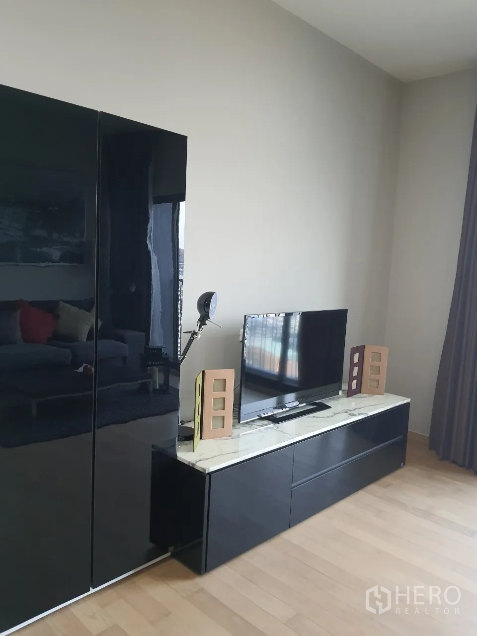 Condominium for rent or sale in Watthana, Bangkok - Living area with flat-screen TV on a marble-top console and glossy black storage cabinet.