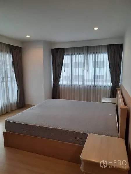 公寓 出租在Watthana, Bangkok - 宽敞卧室，转角窗、大床、床头柜与全遮光窗帘。