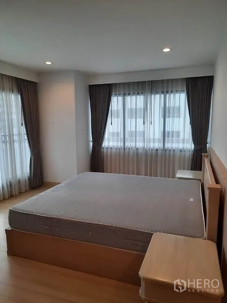 公寓 出租在Watthana, Bangkok - 宽敞卧室，转角窗、大床、床头柜与全遮光窗帘。