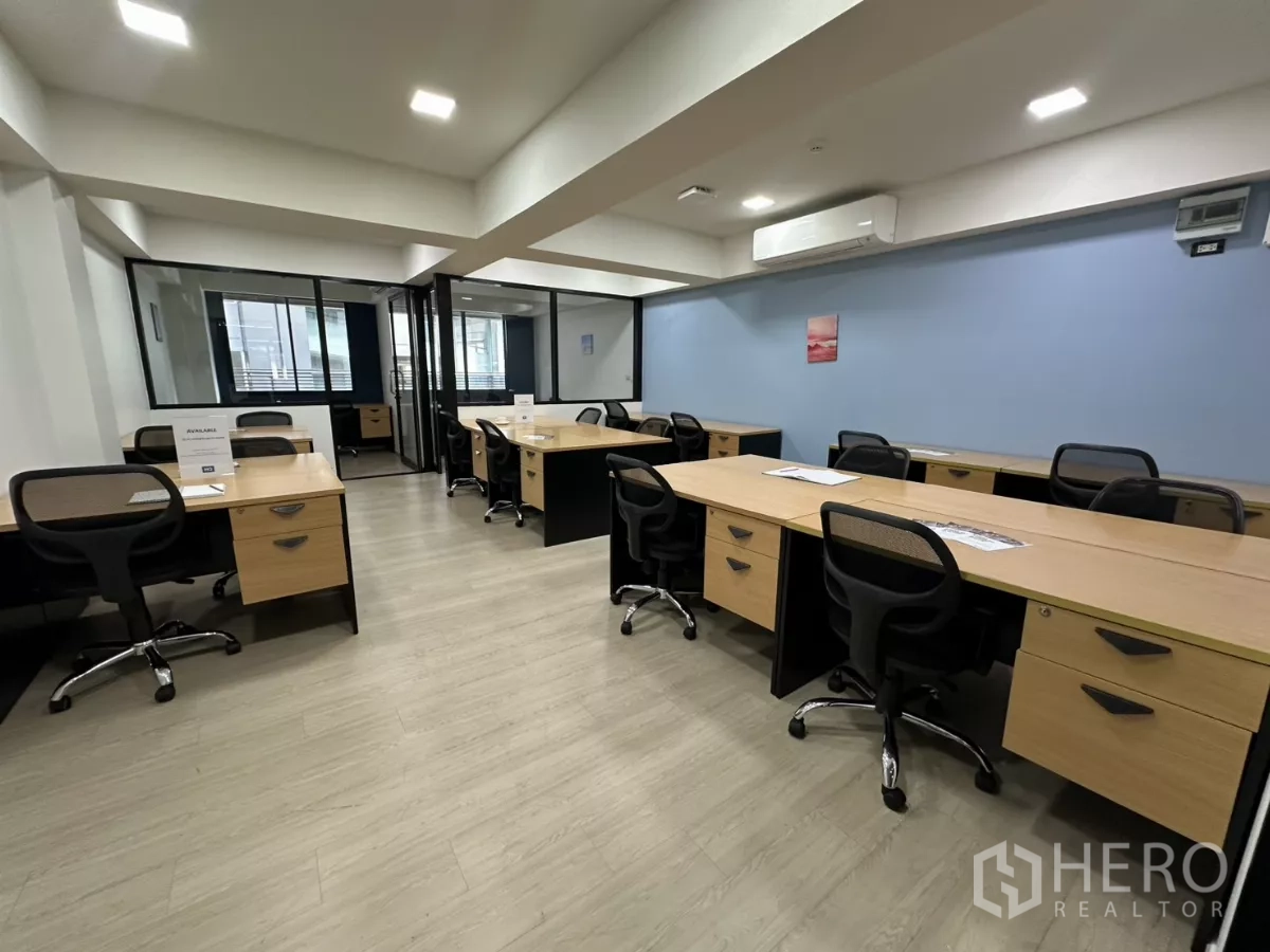 Office Space for rent in Watthana, Bangkok - Open-plan furnished office with multiple workstations, glass partitions, a blue accent wall and air-conditioning.