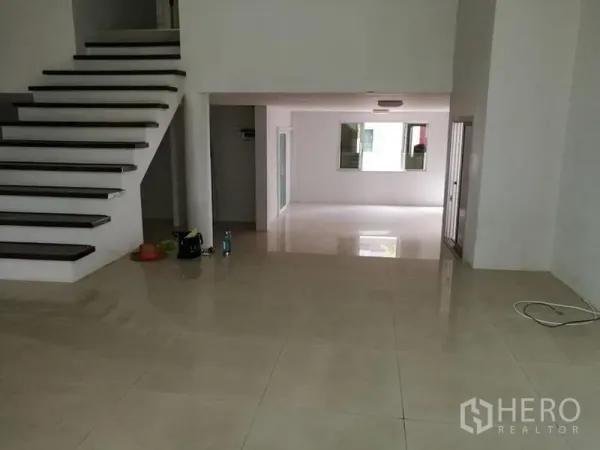 独立式住宅 出租在Phra Khanong, Bangkok - 楼梯旁的错层空间，带通往露台的推拉门与光亮地砖。