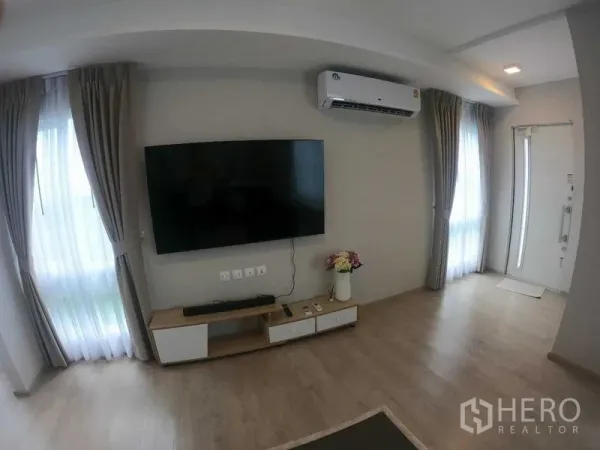 Townhouse for rent - Bright living room with wall-mounted TV, air conditioner, curtains, and light wood flooring.