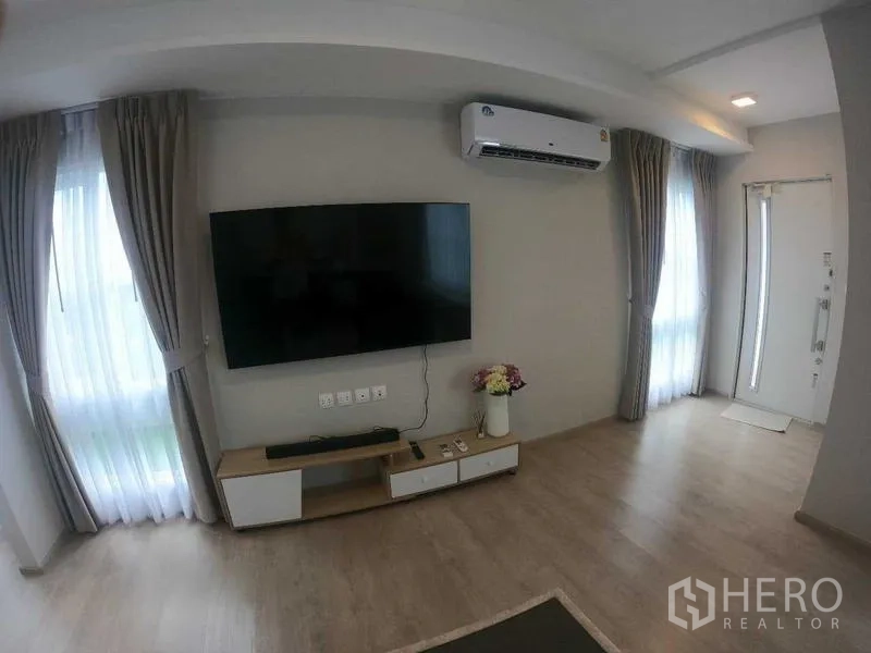 Townhouse for rent - Bright living room with wall-mounted TV, air conditioner, curtains, and light wood flooring.