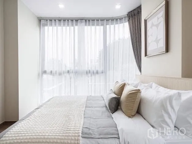 Condominium for rent in Watthana, Bangkok - Bedroom with large window, layered bedding and soft drapes.