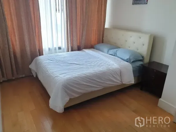 Condominium for rent in Khlong Toei, Bangkok - Cozy bedroom with upholstered bed, wood flooring, bedside table, and large curtained windows.