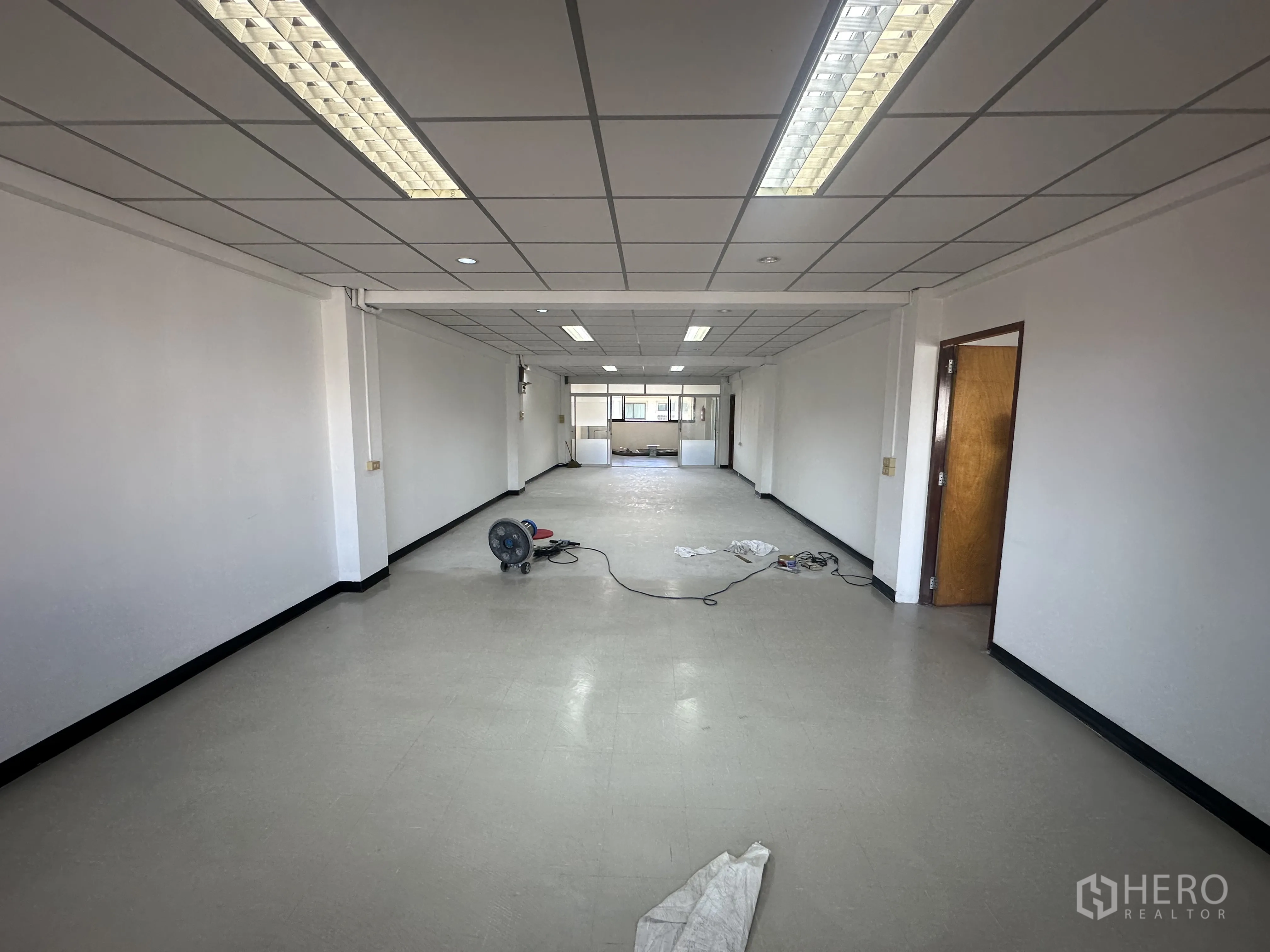 Office Space for rent in Watthana, Bangkok - Spacious empty office floor with white walls, tiled vinyl floor and fluorescent lights leading toward windows.