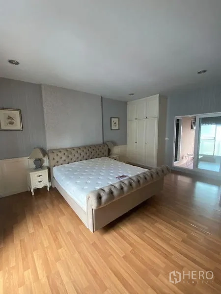 Townhouse for rent in Wang Thonglang, Bangkok - Spacious master bedroom with tufted bed, wardrobes and wood flooring.