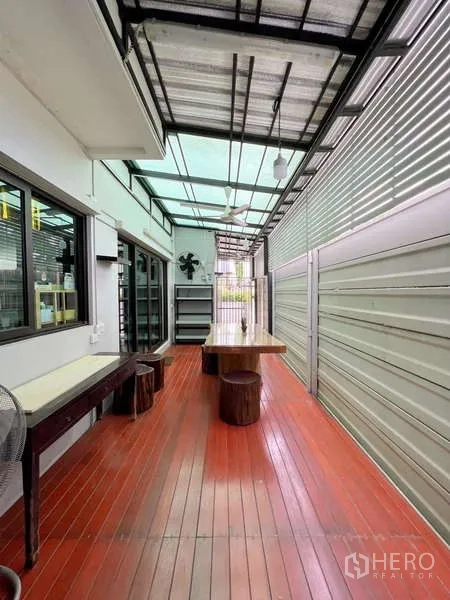 Detached House for sale in Prawet, Bangkok - Covered outdoor deck with long dining table, stools, and translucent roofing for ventilation.