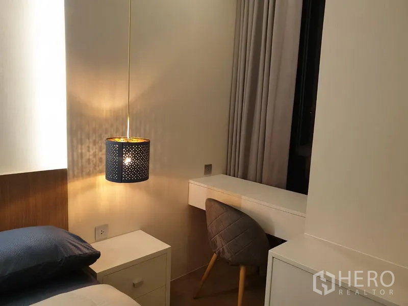 Condominium for rent in Watthana, Bangkok - Bedside pendant light next to a small work desk and chair by the window with curtains.