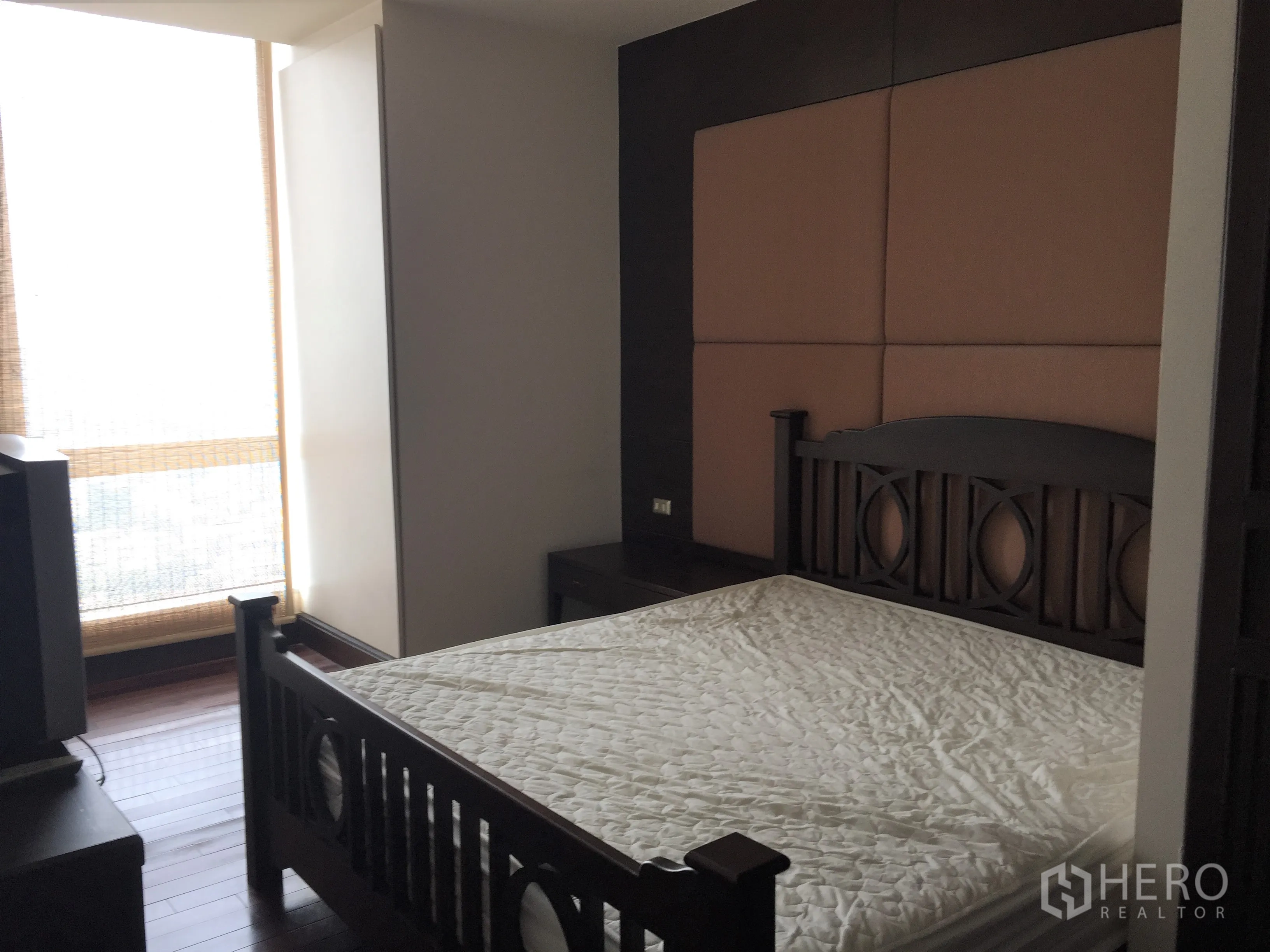 Condominium for rent in Sathon, Bangkok - Master bedroom with queen bed, padded headboard, dark wood furniture, and a floor-to-ceiling window.