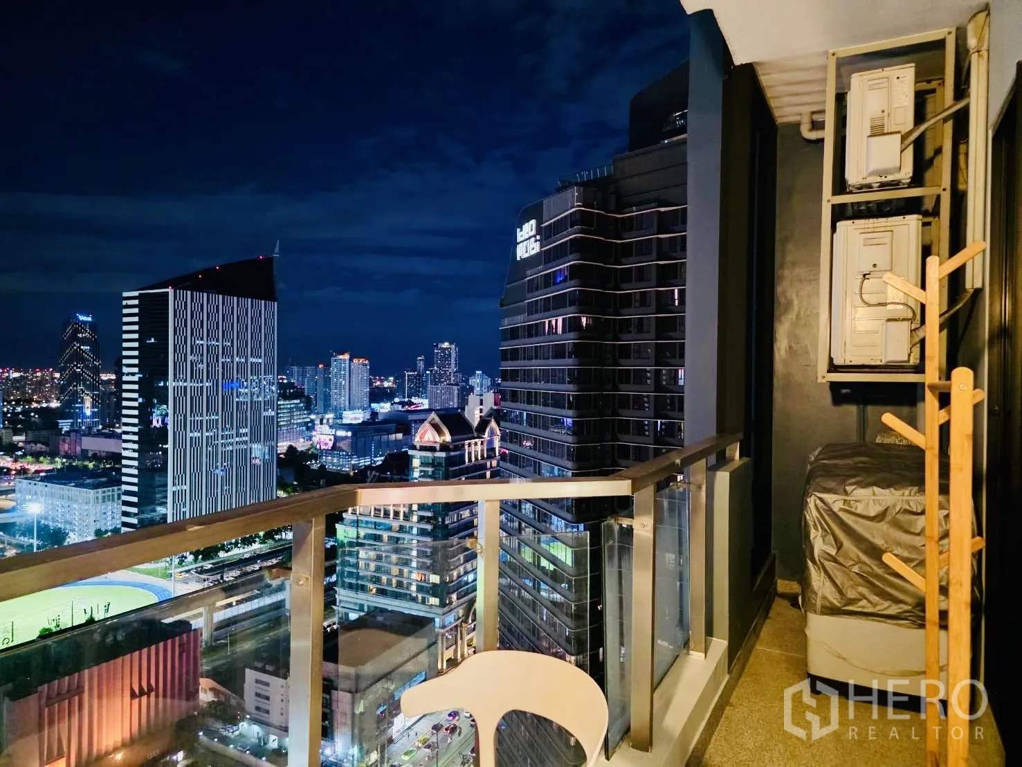 Condominium for rent in Huai Khwang, Bangkok - Balcony corner at night showing air-conditioning units and neighboring towers.