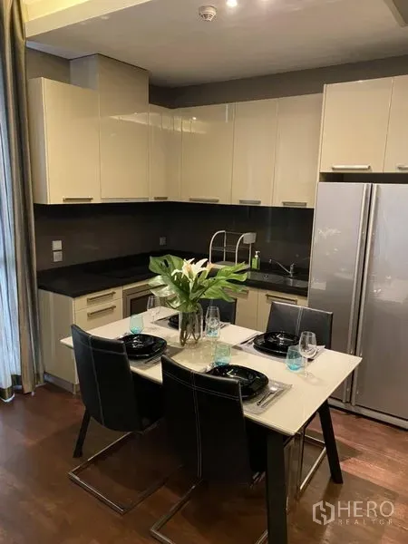 公寓 出租在Watthana, Bangkok - 现代厨房配亮面橱柜、黑色台面、双开门冰箱及四人餐桌。