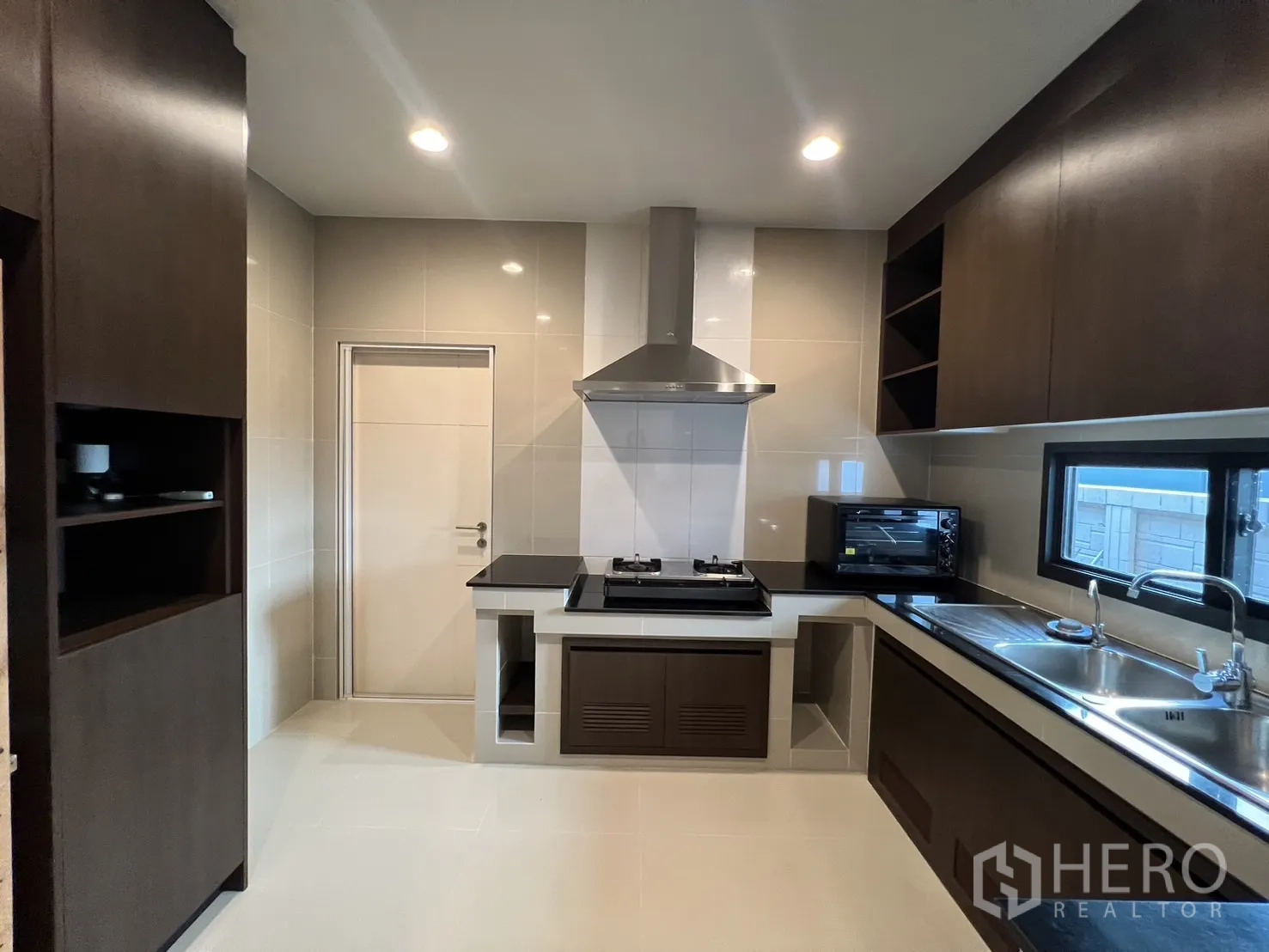 Detached House for rent or sale in Bang Kapi, Bangkok - Built‑in kitchen featuring gas hob, chimney hood and dark wood cabinetry.