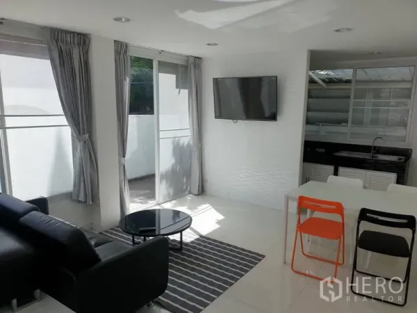 Detached House for rent in Khlong Toei, Bangkok - Open-plan living and dining area with wall-mounted TV, sliding glass doors and compact dining set.