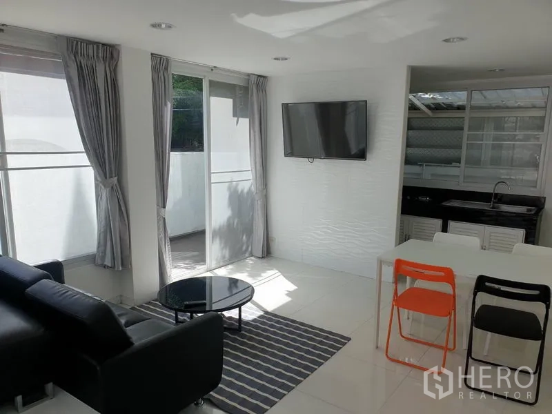 Detached House for rent in Khlong Toei, Bangkok - Open-plan living and dining area with wall-mounted TV, sliding glass doors and compact dining set.