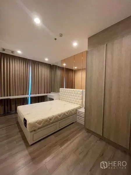 คอนโด ให้เช่า - ห้องนอนหลักเตียงหุ้มหนัง ผนังกระจก ตู้เสื้อผ้าบิวท์อิน พื้นไม้ และผ้าม่านทึบ