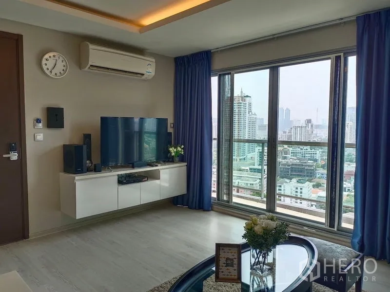 คอนโด ให้เช่าในWatthana, Bangkok - ห้องนั่งเล่นมีชั้นวางทีวีและประตูหน้าต่างสูงจรดเพดานเปิดสู่ระเบียงวิวเมือง