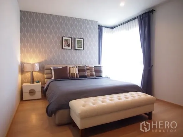 คอนโด ขายในWatthana, Bangkok - ห้องนอนใหญ่ผนังลายวอลเปเปอร์ หน้าต่างบานใหญ่พร้อมม่านโปร่ง และม้านั่งปลายเตียงหุ้มเบาะ