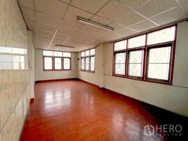 Shophouse for rent in Sathon, Bangkok - Bright room with multiple windows and patterned grilles, glossy wooden floor and fluorescent lighting.