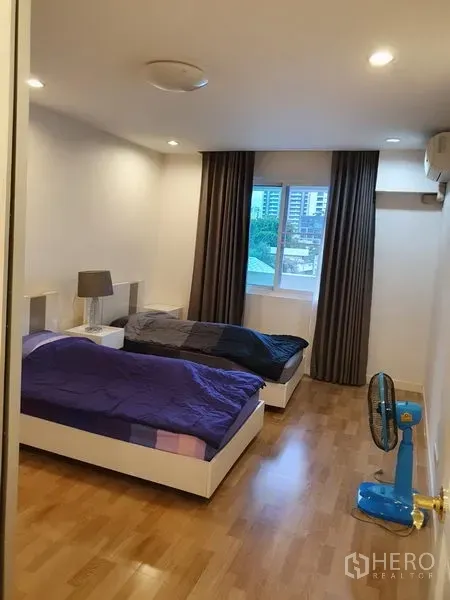 Condominium for rent in Watthana, Bangkok - Bright bedroom with two single beds, wood floors, window with city view, and blackout curtains.