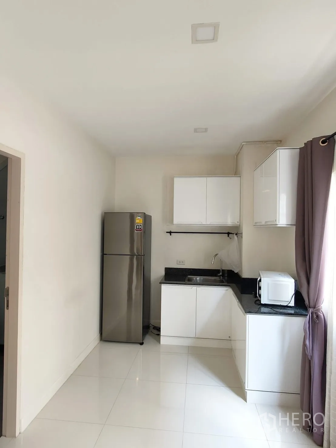 Townhouse for rent in Saphan Sung, Bangkok - Compact white kitchen with granite countertop, sink, fridge, microwave and cabinets.