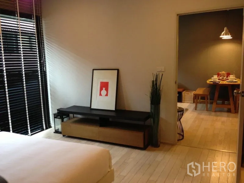 公寓 出租在Watthana, Bangkok - 从卧室望向餐区，电视柜与装饰画，大窗配百叶，木地板通透。