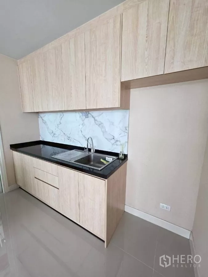 Detached House for rent or sale in Samut Prakan - Western kitchen with light wood cabinetry, black countertop and marble backsplash.