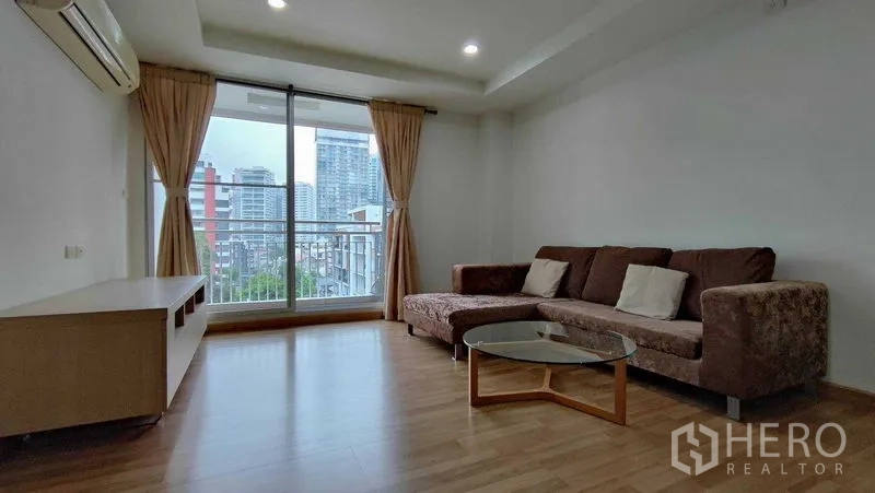 คอนโด ให้เช่าในKhlong Toei, Bangkok - โซนรับแขกพร้อมโซฟาเข้ามุม โต๊ะกลาง และประตูกระจกบานเลื่อนเปิดสู่วิวตึกสูง