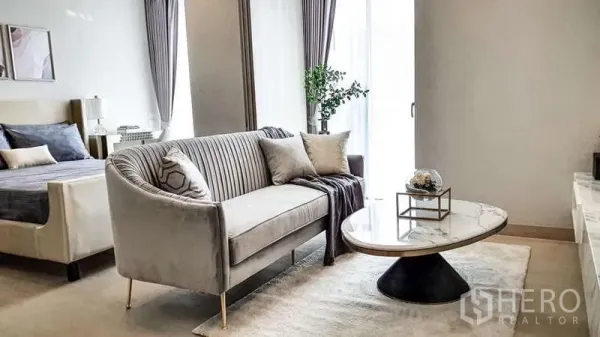 Condominium for sale in Khlong Toei, Bangkok - Contemporary living zone with curved sofa, round marble table, and sliding door to a bright window space.
