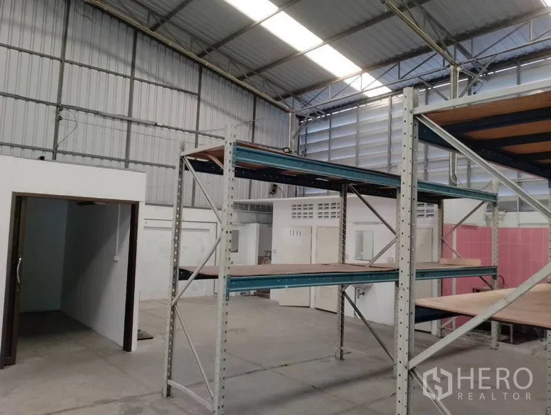 Warehouse for rent in Huai Khwang, Bangkok - Corner of warehouse showing shelving units, service room doors and smooth concrete floor.