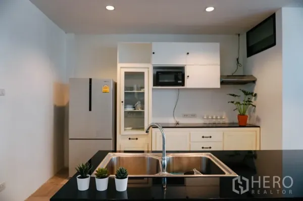 Townhouse for rent in Watthana, Bangkok - Modern kitchen with white cabinetry, black countertops, island sink and a stainless refrigerator.