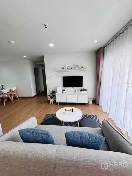 Condominium for rent in Watthana, Bangkok - Open living area facing the TV cabinet and balcony, with wood floors and a patterned rug.