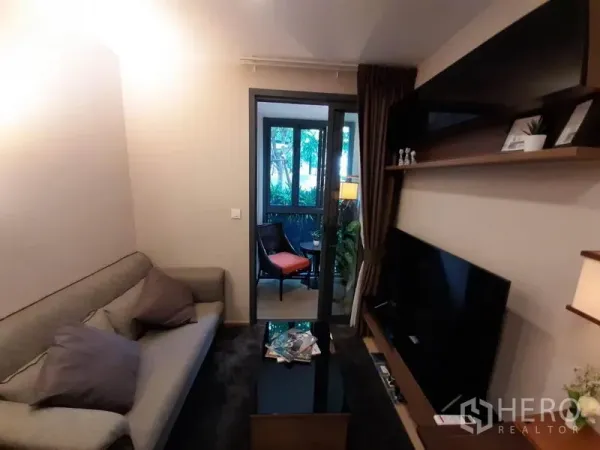 公寓 出租或出售在Watthana, Bangkok - 客厅配沙发与电视墙，推拉玻璃门通向绿意阳台。