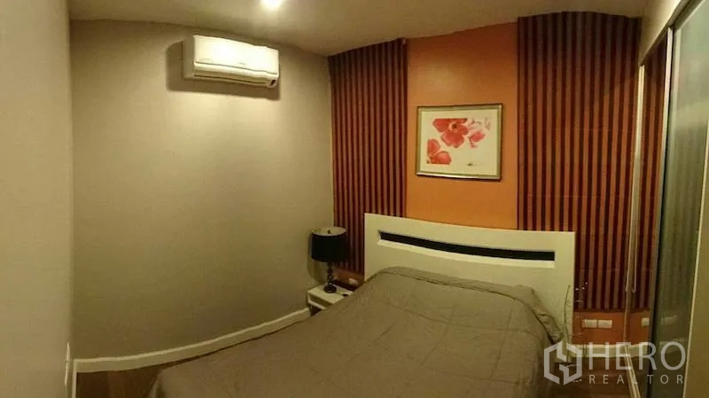 Condominium for rent or sale in Watthana, Bangkok - Cozy bedroom with warm accent wall, bedside table and wall-mounted air conditioner.