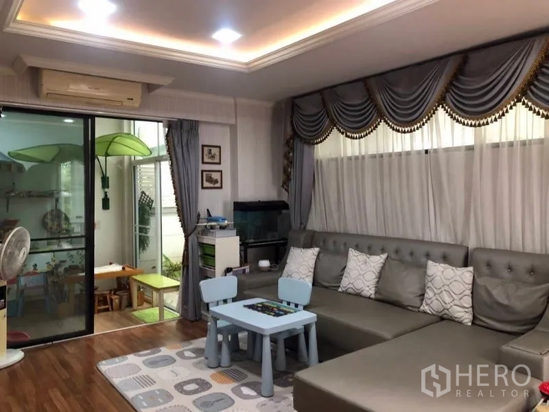 บ้าน ขายในLam Luk Ka, Pathum Thani - ห้องนั่งเล่นครอบครัว โซฟาตัวยาว พื้นที่มุมเด็กเล่น และประตูกระจกสไลด์เชื่อมซันรูม.