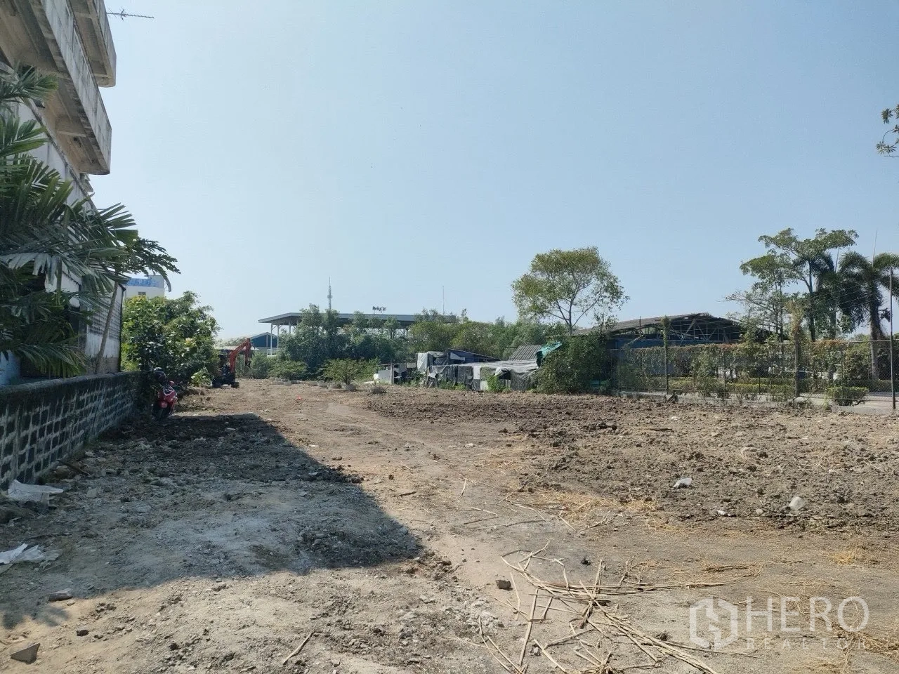 Land for sale in Mueang Samut Prakan, Samut Prakan - Vacant land corridor beside a building, cleared soil and excavator at the far end.