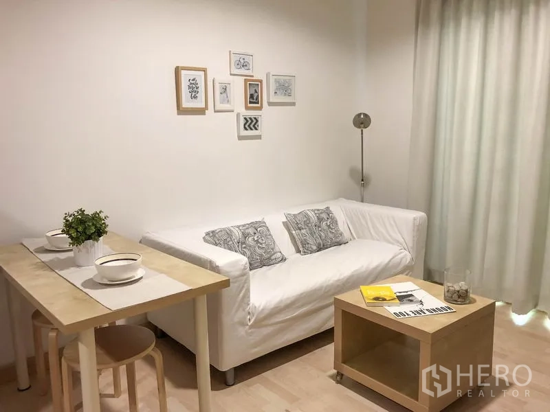 公寓 出租或出售在Watthana, Bangkok - 温馨客厅，白色沙发、墙面装饰画、双人餐桌与高挑窗帘。