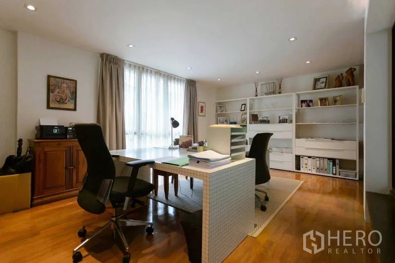 Home Office for sale in Watthana, Bangkok - Dedicated office room with large workstation, shelving and natural light through curtains.