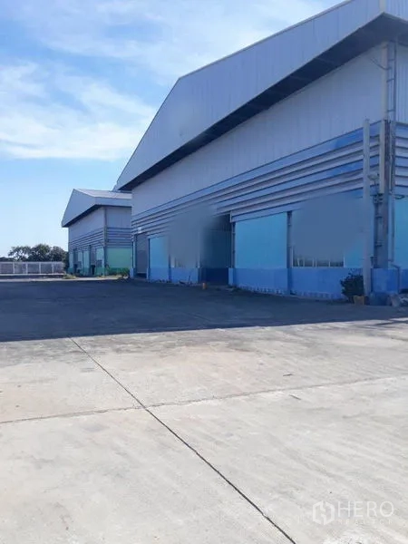 工厂 出租在Samut Prakan - 蓝灰色厂房正立面，前方为宽大装卸区。