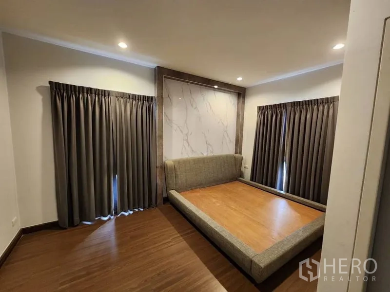 Detached House for rent in Prawet, Bangkok - Second bedroom with platform bed, marble accent wall, wood flooring and curtains.