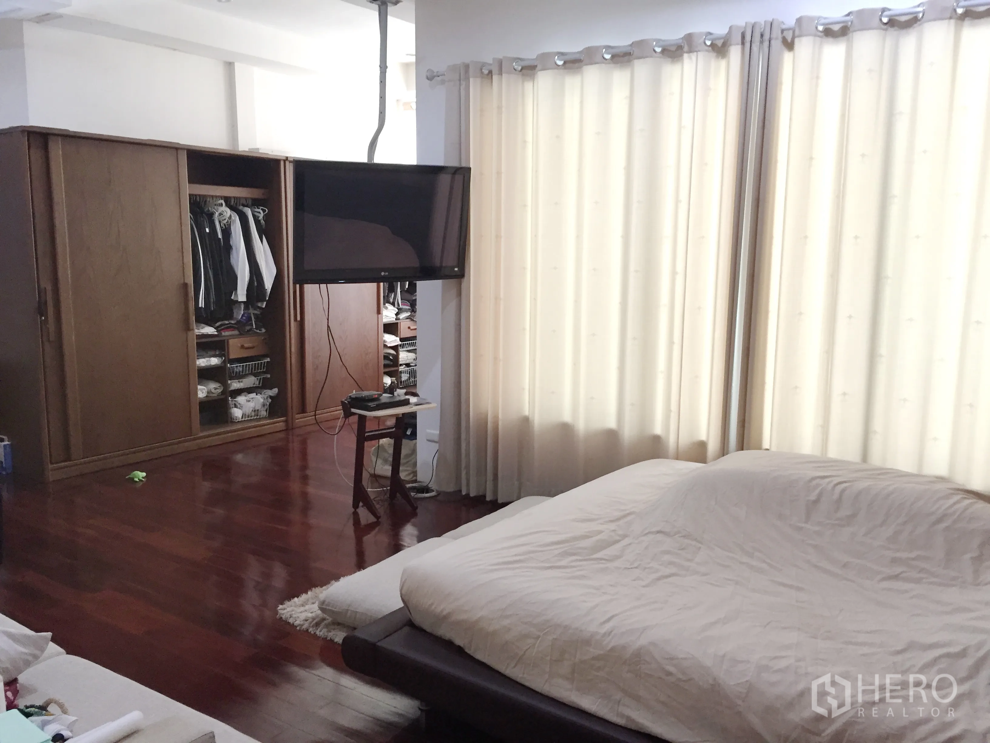 Townhouse for rent in Khlong Toei, Bangkok - Master bedroom with large bed, wall‑mounted TV, wardrobe and floor‑length curtains on polished wood floors.