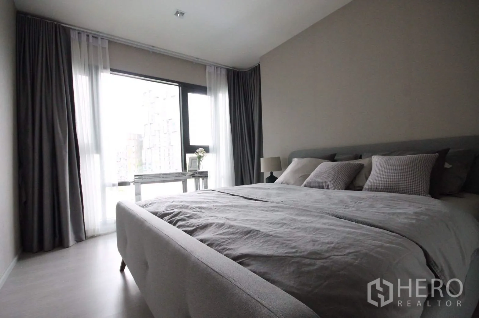Condominium for rent in Khlong Toei, Bangkok - Master bedroom with king bed, soft grey linens and a wide window offering city views beside a small desk.