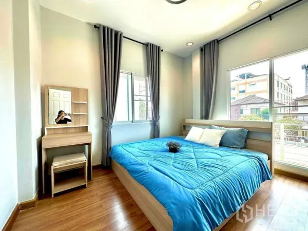 บ้าน ให้เช่าในLat Krabang, Bangkok - ห้องนอนสว่างพร้อมหน้าต่างบานใหญ่ ผ้าม่านสีเทา พื้นไม้ เตียงผ้าปูสีน้ำเงินและโต๊ะเครื่องแป้ง