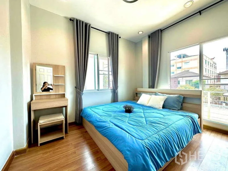 บ้าน ให้เช่าในLat Krabang, Bangkok - ห้องนอนสว่างพร้อมหน้าต่างบานใหญ่ ผ้าม่านสีเทา พื้นไม้ เตียงผ้าปูสีน้ำเงินและโต๊ะเครื่องแป้ง